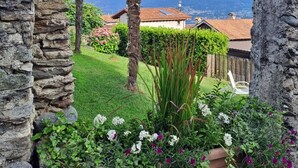 A stone archway framing a garden with a palm tree, potted plants, and a mountain view. - 2 1/2-room vacation apartment in Vercana, quiet and inviting above Lake Como (Vercana)