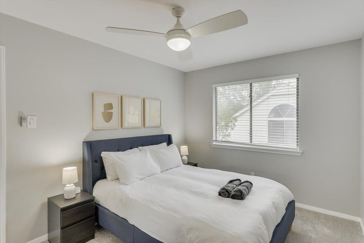 A bedroom with a bed, nightstands, a ceiling fan, and a window with blinds.
