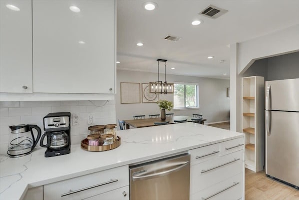 A modern kitchen with white cabinetry, a built-in dishwasher, and a coffee maker.