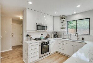 A modern kitchen with white cabinetry, a built-in microwave, a gas stove, and a large window. - Perfect Getaway Home w 5 Bedrooms & Backyard Oasis (Plano)
