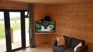 A cozy living room with a wooden interior, a grey sofa, and a flat-screen TV mounted on the wall.