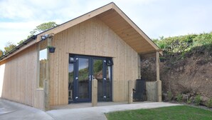 A wooden building with a sloped roof, large glass doors, and a concrete pathway leading to the entrance.