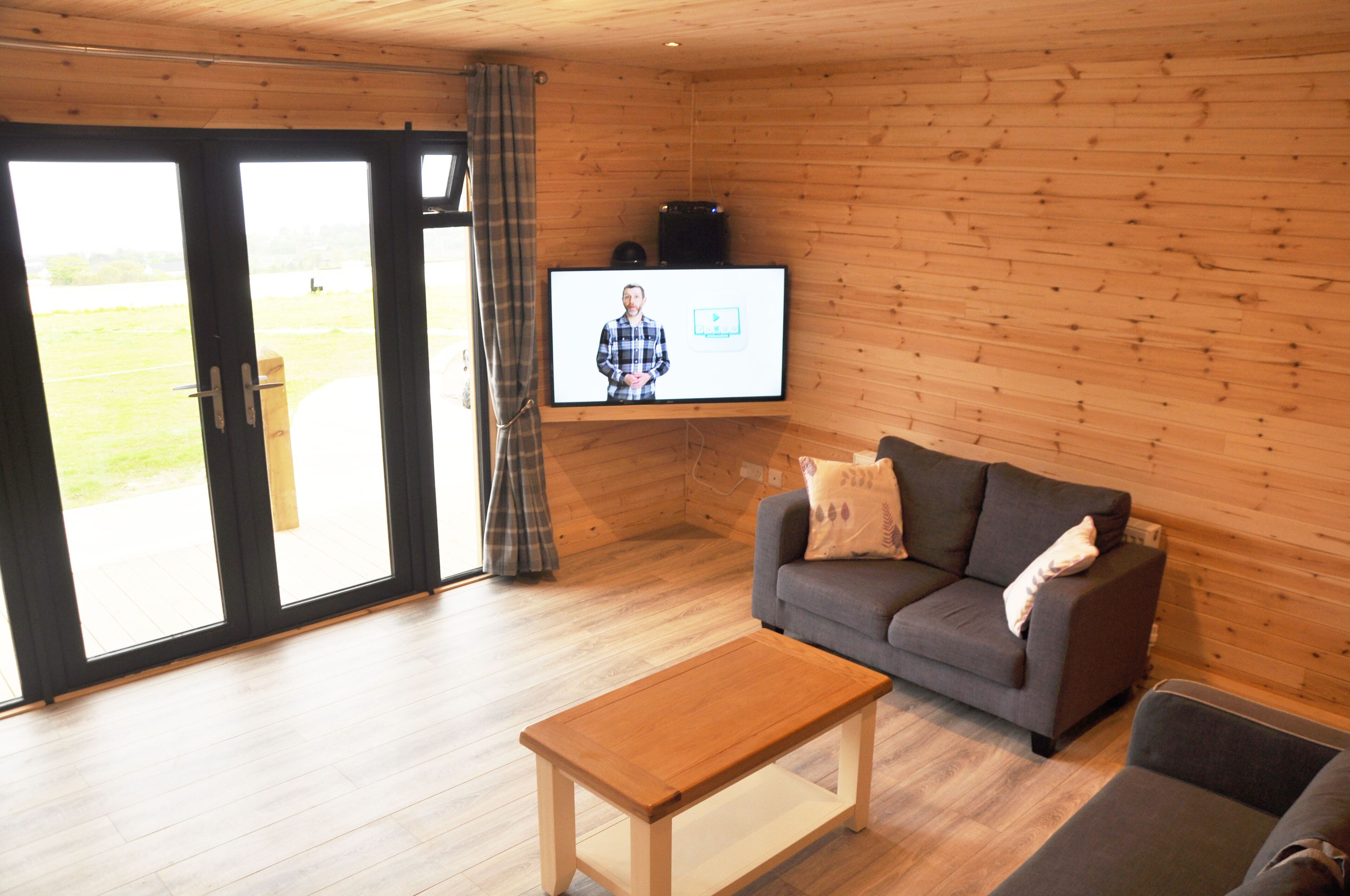 A modern living room with a wooden floor, a grey sofa, a wooden coffee table, and a TV mounted on the wall.