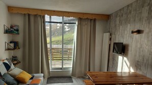 A cozy room with a wooden table, a sofa with patterned cushions, a TV mounted on the wall, and a large window with curtains. - Studio cabin Piau Engaly, at the foot of the slopes (Piau-Engaly)