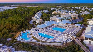 A resort with multiple swimming pools, a large covered area, and a view of the surrounding forest and water.