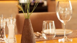 Une table à manger ornée d’un vase de fleurs jaunes, de salières et de poivrières, et d’un verre à vin.