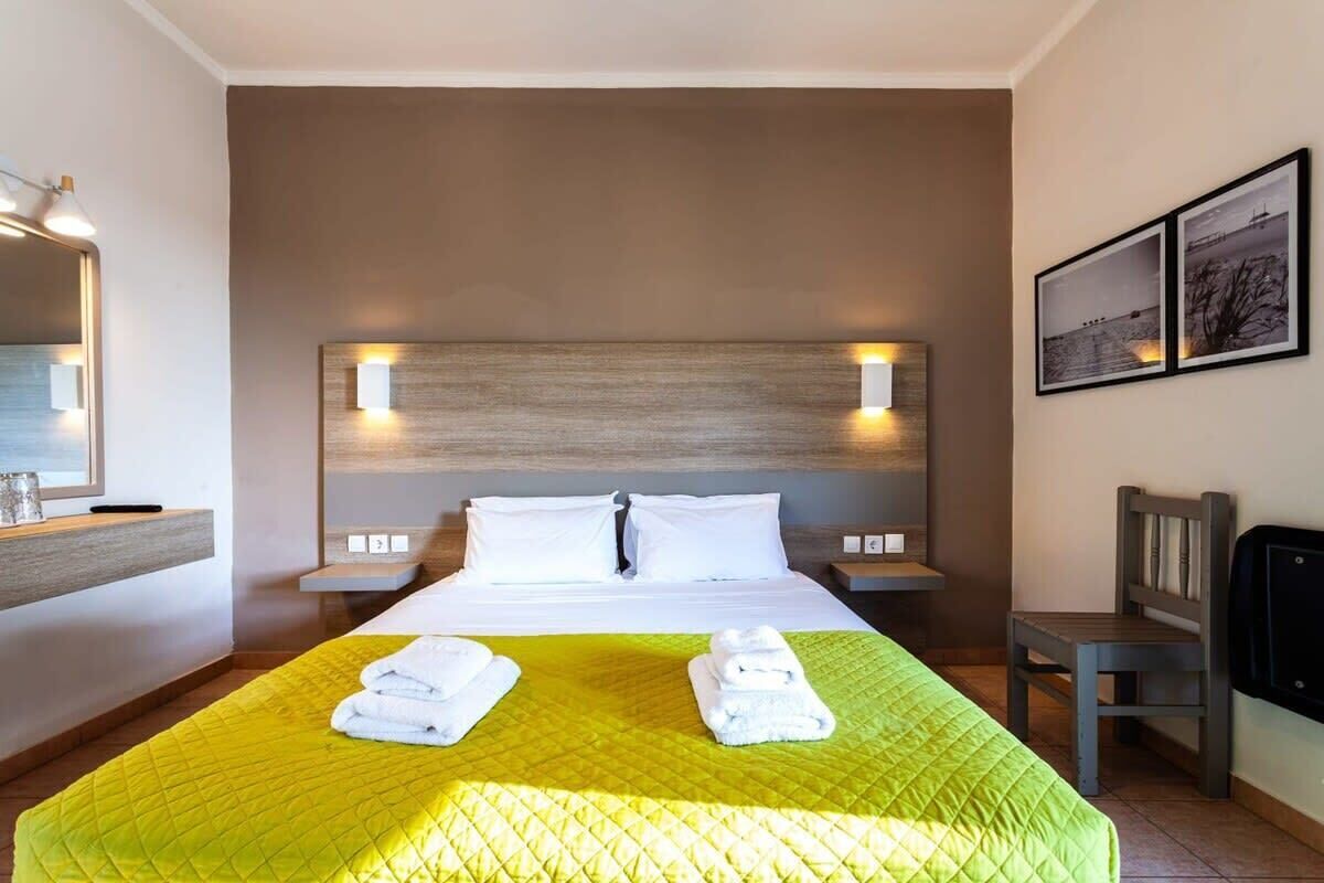 Ein Hotelzimmer mit einem großen Bett, zwei Nachttischen, einem Sessel und einem an der Wand montierten Fernseher.