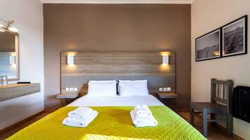 Ein Hotelzimmer mit einem großen Bett, zwei Nachttischen, einem Sessel und einem an der Wand montierten Fernseher.
