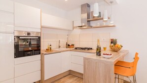A modern kitchen with white cabinets, a built-in oven, a gas stove, and a wooden countertop. There is a bar area with a bottle of champagne and a bowl of fruit.