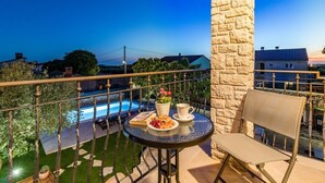 A balcony with a round table, a chair, a potted plant, and a view of a swimming pool.