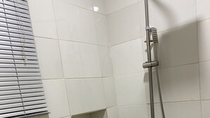Et lille badeværelse med fliser, en bruser, toilet og en hylde med toiletartikler.