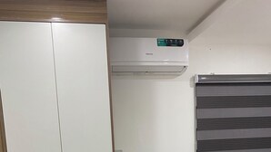 Et værelse med et hvidt skab, en fastgjort aircondition, et fladskærms-tv og et træskrivebord.