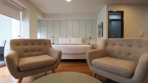 A bedroom with a bed, two armchairs, a round table, and a nightstand.