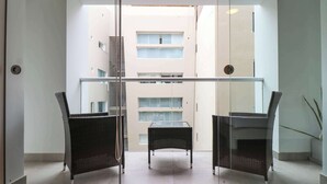 A modern interior with two wicker chairs and a small table, a glass partition, and a view of a building with multiple windows.