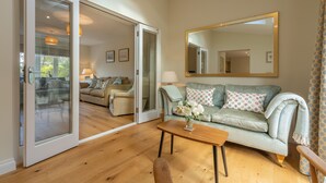 A living room with a sliding glass door leading to a balcony, a light green sofa with patterned cushions, a wooden coffee table, and a large mirror on the wall. - The Sidings, Docking, Norfolk (Docking)