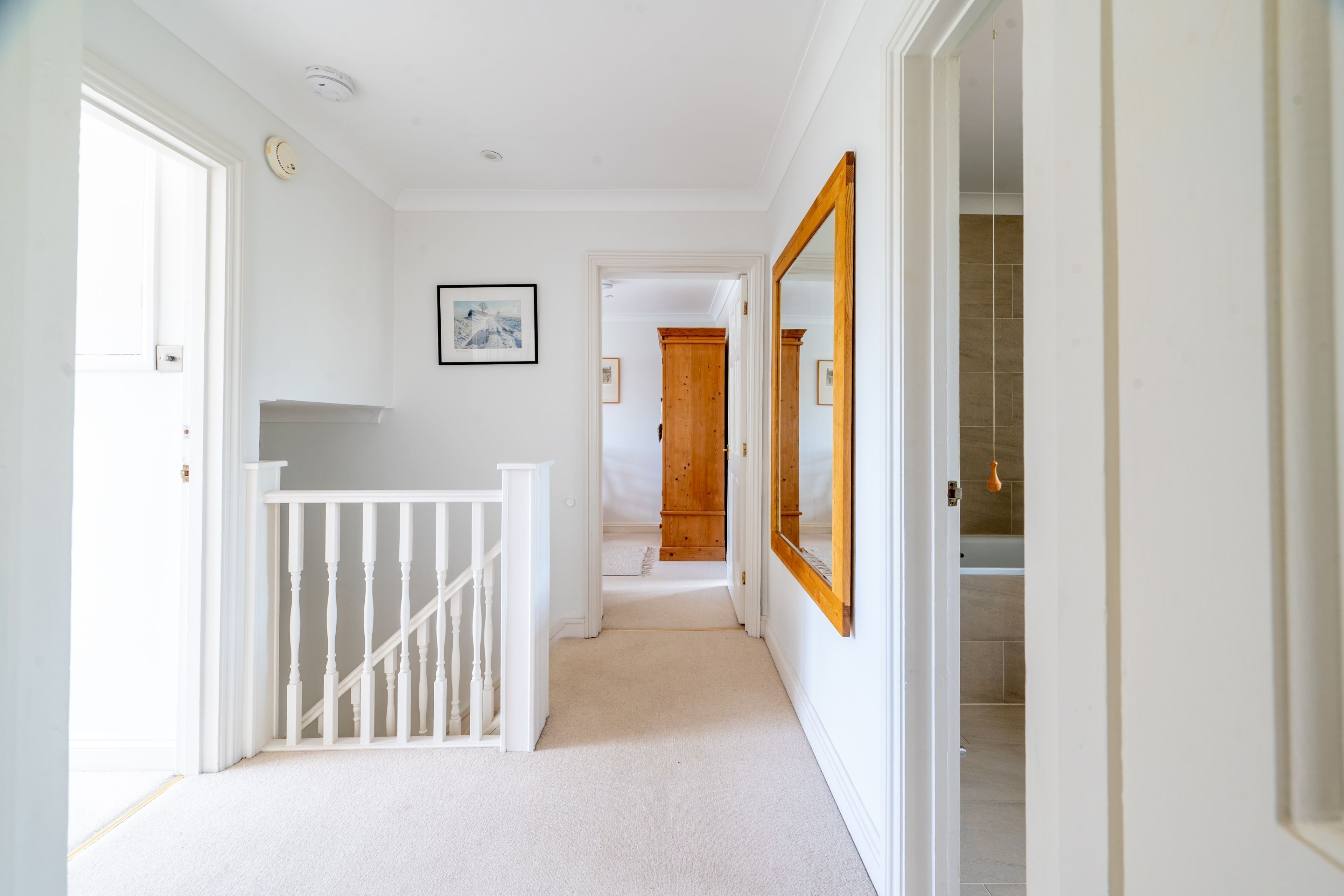 A hallway with white walls, a wooden door, and a white railing.