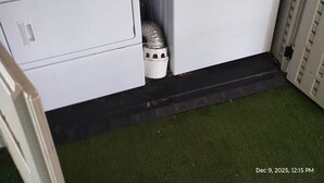 Un cuarto de lavandería con dos lavadoras y secadoras apiladas, un bote de basura y un estante metálico con cajas.