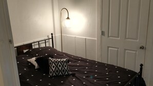 Un dormitorio con cama, mesita de noche, lámpara de pared y una puerta.