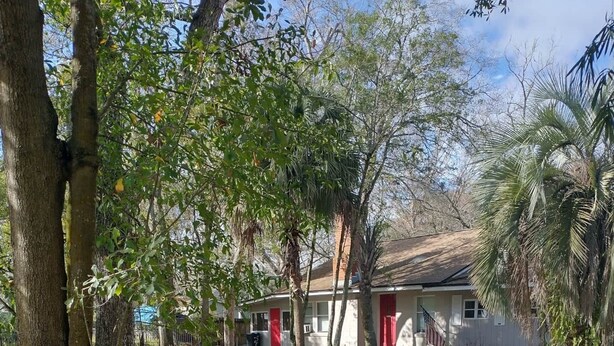 Un barrio residencial con una casa que tiene una puerta roja, rodeada de árboles y un camino de grava.