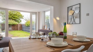 Uma sala de jantar com uma mesa de madeira posta para quatro pessoas, um sofá e um quadro na parede.