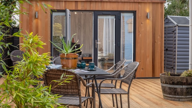 Um deck de madeira com uma mesa e cadeiras, rodeado por plantas em vasos.