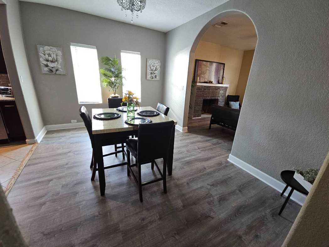 A dining area with a table set for four, a fireplace, and a staircase leading to another level.