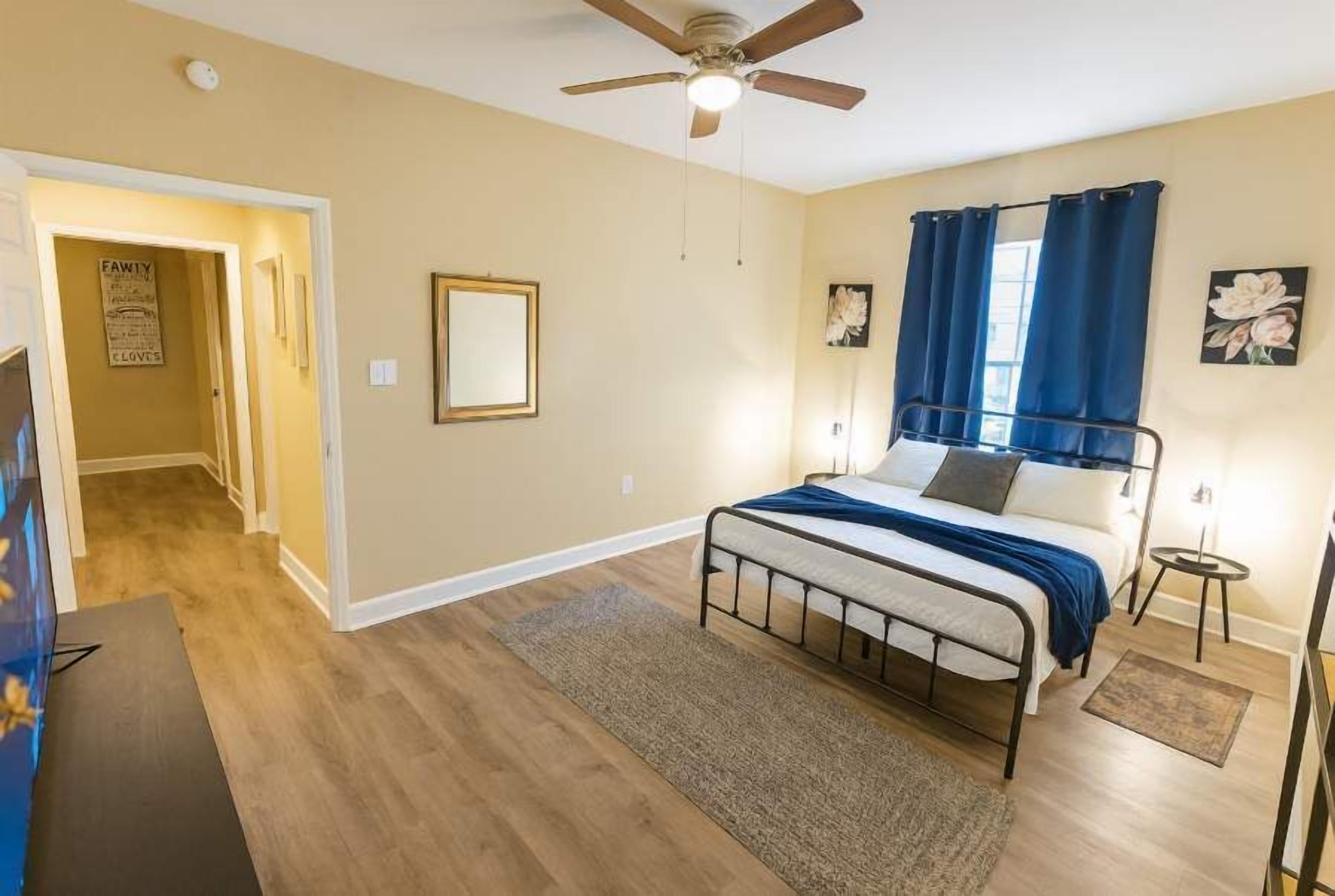 A bedroom with a bed, a ceiling fan, a nightstand, and a door leading to another room.