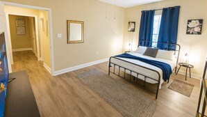 Ein Schlafzimmer mit einem Bett, einem Deckenventilator, einem Nachttisch und einer Tür zu einem anderen Raum.