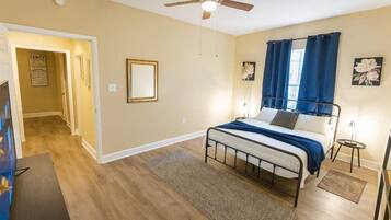 A bedroom with a bed, a ceiling fan, a nightstand, and a door leading to another room.