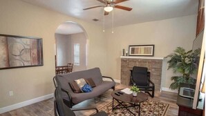 Ein Wohnzimmer mit Sofa, Sesseln, einem Couchtisch, einem Kamin und einem Deckenventilator.