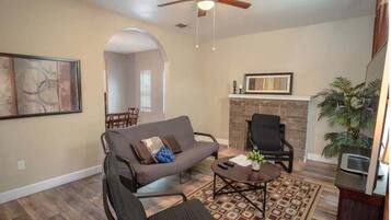 A living room with a sofa, armchairs, a coffee table, a fireplace, and a ceiling fan.