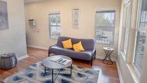 Ein Wohnzimmer mit einem grauen Sofa, einem kleinen runden Couchtisch und einem gemusterten Teppich.
