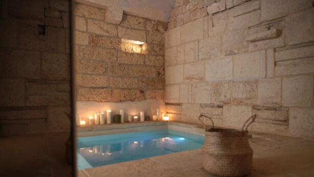 A stone-walled room with a pool, candles, and a woven basket. - Lanime _ Bed in Spa _ (Sogliano Cavour)