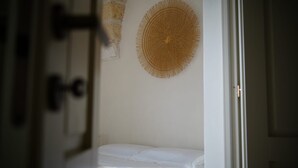 A room with a white bed, a woven wall hanging, and a door with a handle. - Lanime _ Bed in Spa _ (Sogliano Cavour)