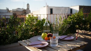 A table set outdoors with fruits, a bottle, and glasses, overlooking a garden and buildings. - Lanime _ Bed in Spa _ (Sogliano Cavour)