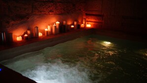 A hot tub with candles in a stone-walled room. - Lanime _ Bed in Spa _ (Sogliano Cavour)