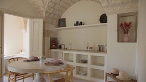 A dining area with a round table, chairs, and a white ceiling with stonework. Shelves with dishes and a vase with dried flowers are visible. - Lanime _ Bed in Spa _ (Sogliano Cavour)