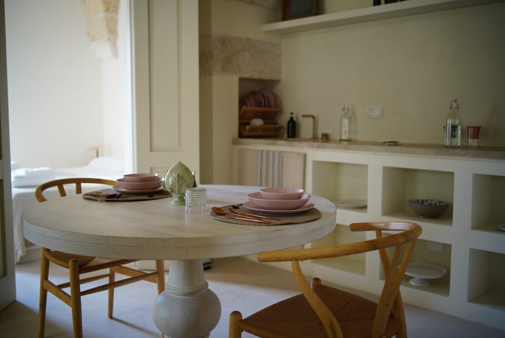 A round dining table with pink plates and a green pitcher, surrounded by wooden chairs.