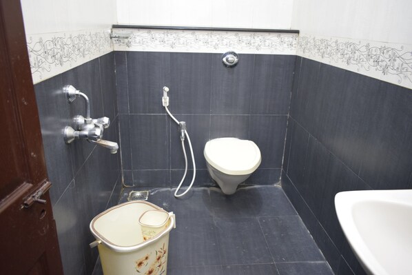 A bathroom with dark tiles, a toilet, a shower, and a sink.