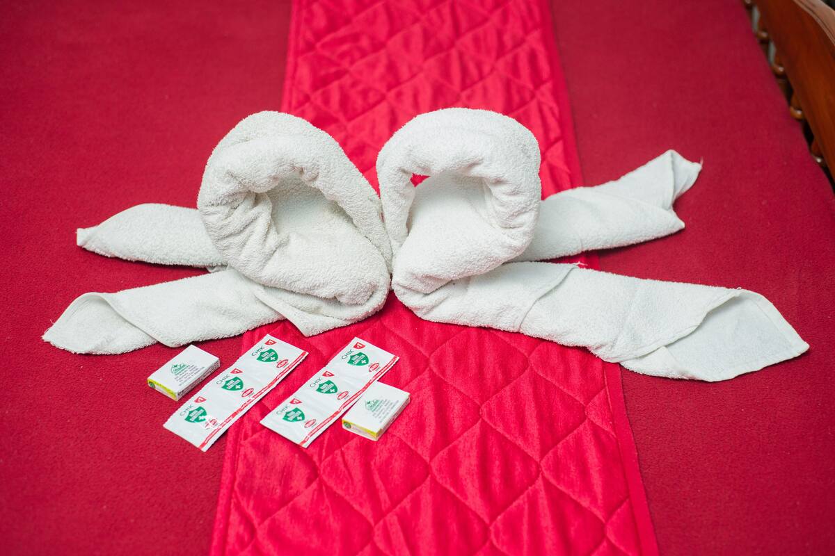 Una cama con una colcha acolchada roja, dos toallas blancas dispuestas en forma de lazo y cuatro tarjetas pequeñas con diseños verdes y blancos.