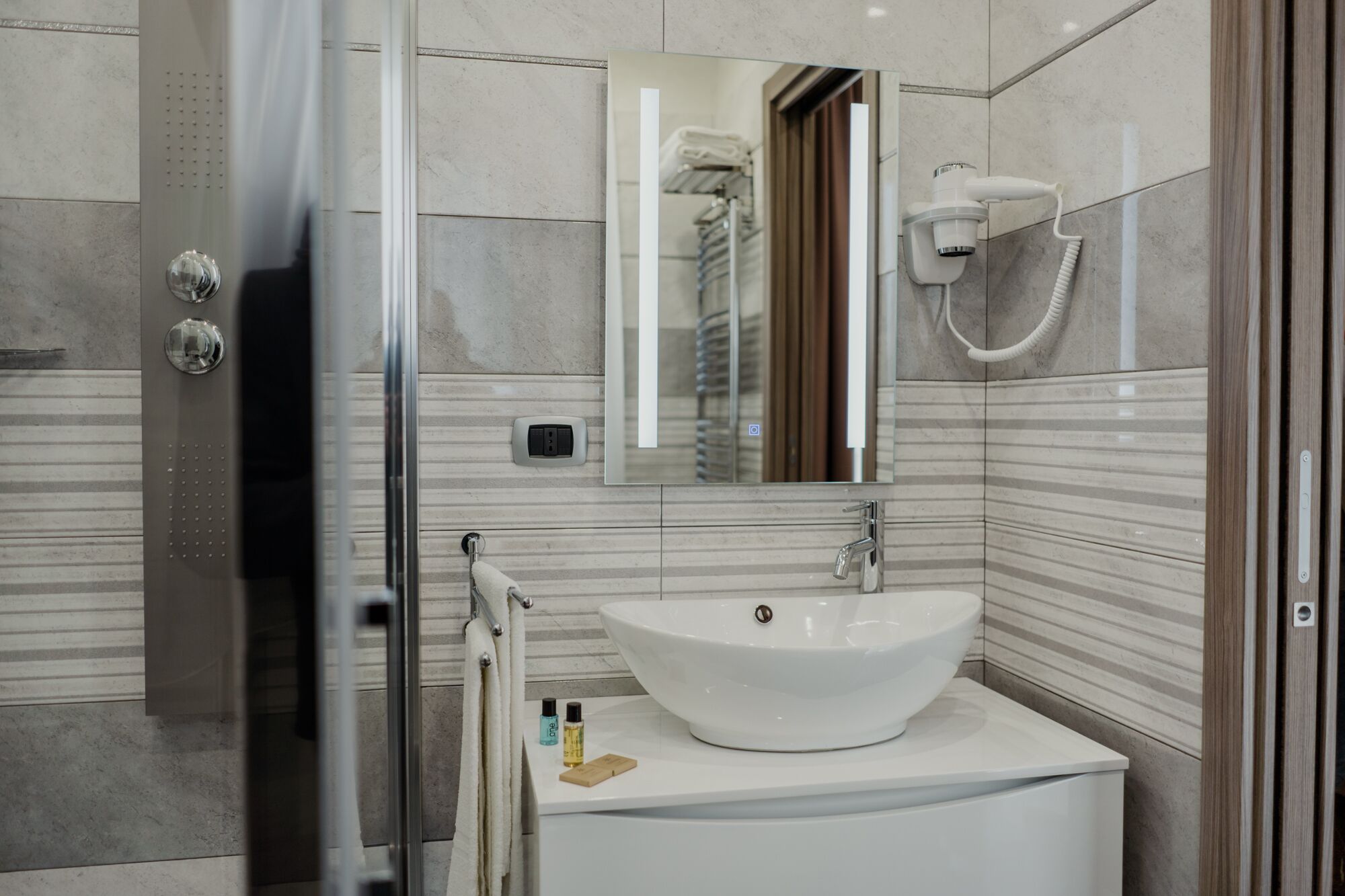 A modern bathroom with a glass shower enclosure, a white sink with a vessel basin, and a mirror above the sink.