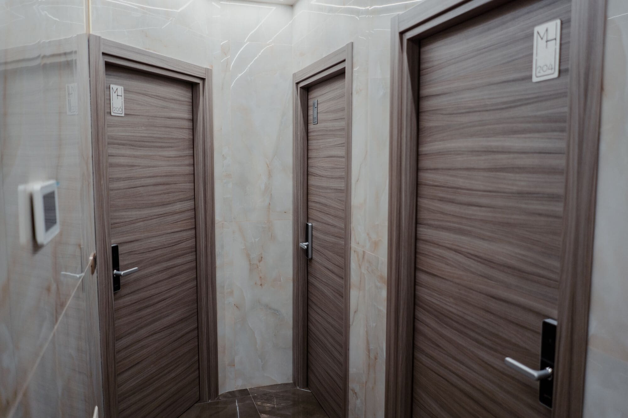 A hallway with three closed doors, each with a metal handle and a small label above the handle.