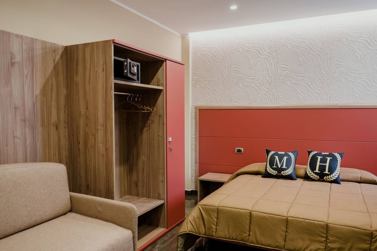 A bedroom with a bed, a wardrobe, and a seating area.