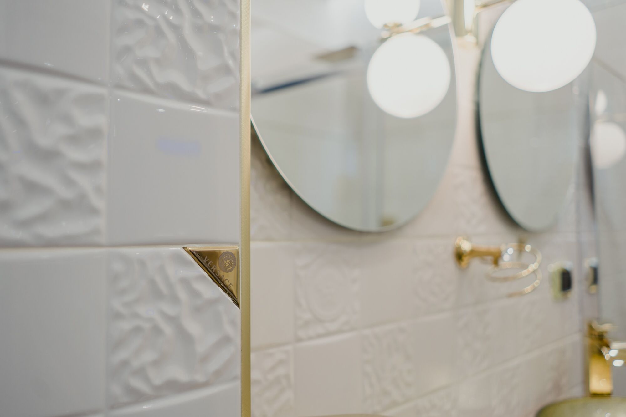 Une salle de bain avec des carreaux blancs à texture, un miroir à cadre doré et un robinet doré.