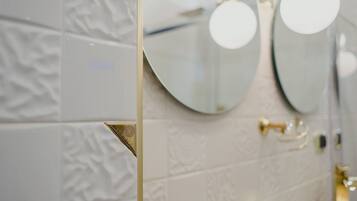 Une salle de bain avec des carreaux blancs à texture, un miroir à cadre doré et un robinet doré.
