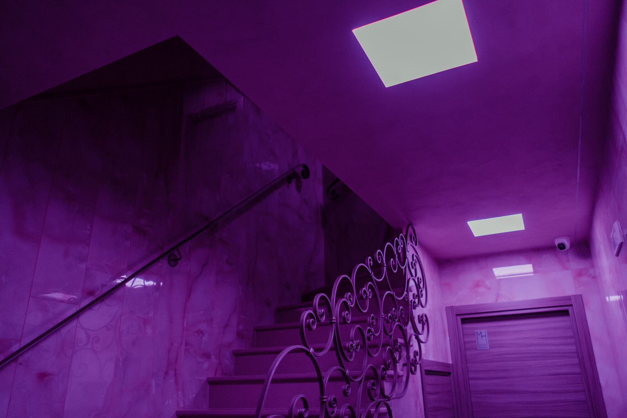 A purple-lit stairwell with a metal railing and a door at the bottom.