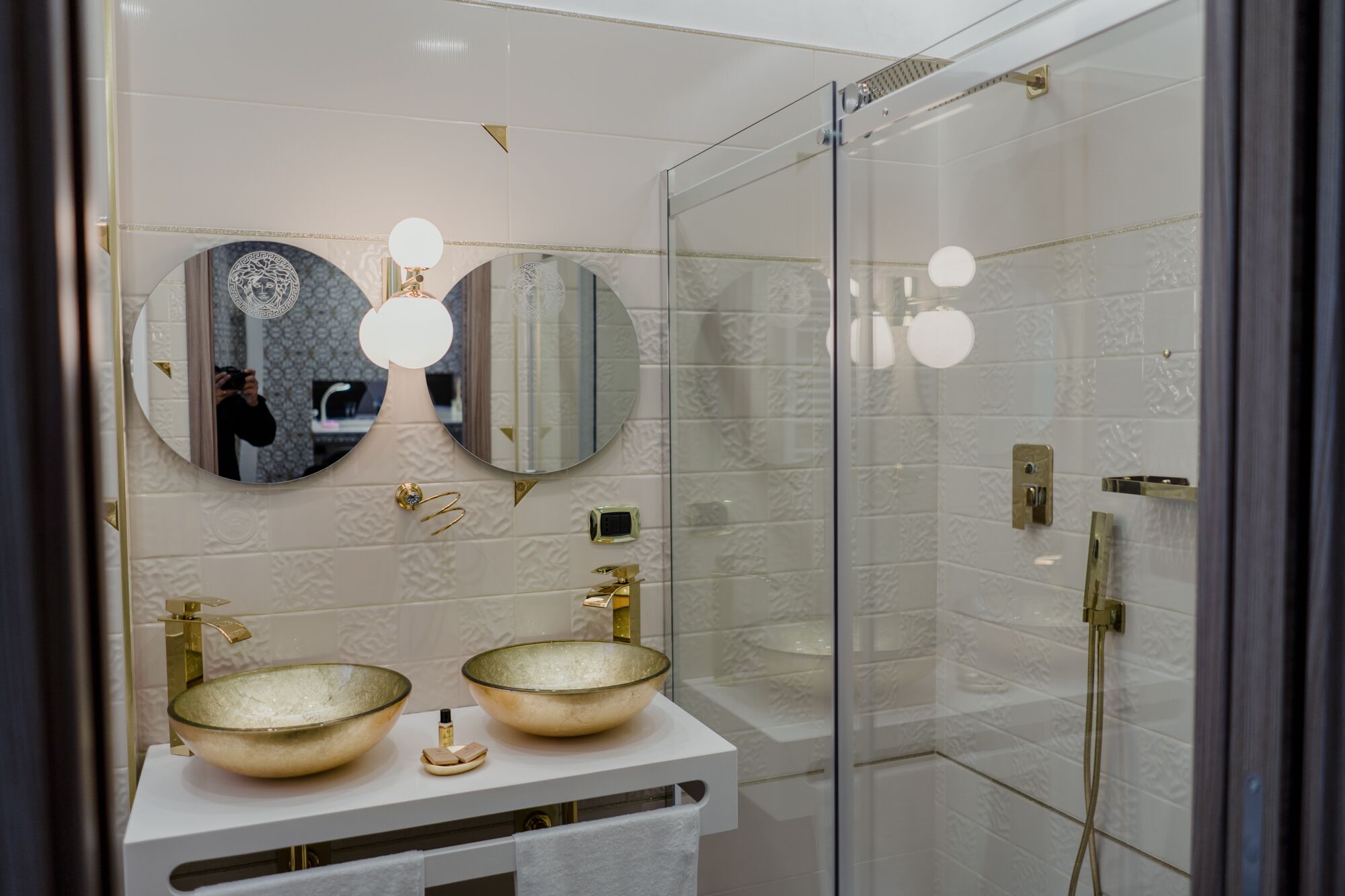 Ein modernes Badezimmer mit zwei großen Glaswaschbecken, einer begehbaren Dusche und einem großen Spiegel mit runden Leuchten.