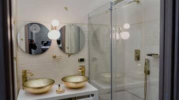 A modern bathroom with two large glass sinks, a walk-in shower, and a large mirror with round lights.