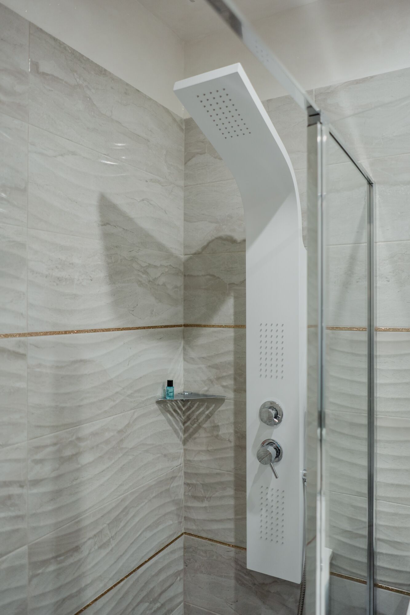 Una doccia moderna con design curvo, porta in vetro e piccolo ripiano con articoli da toilette.