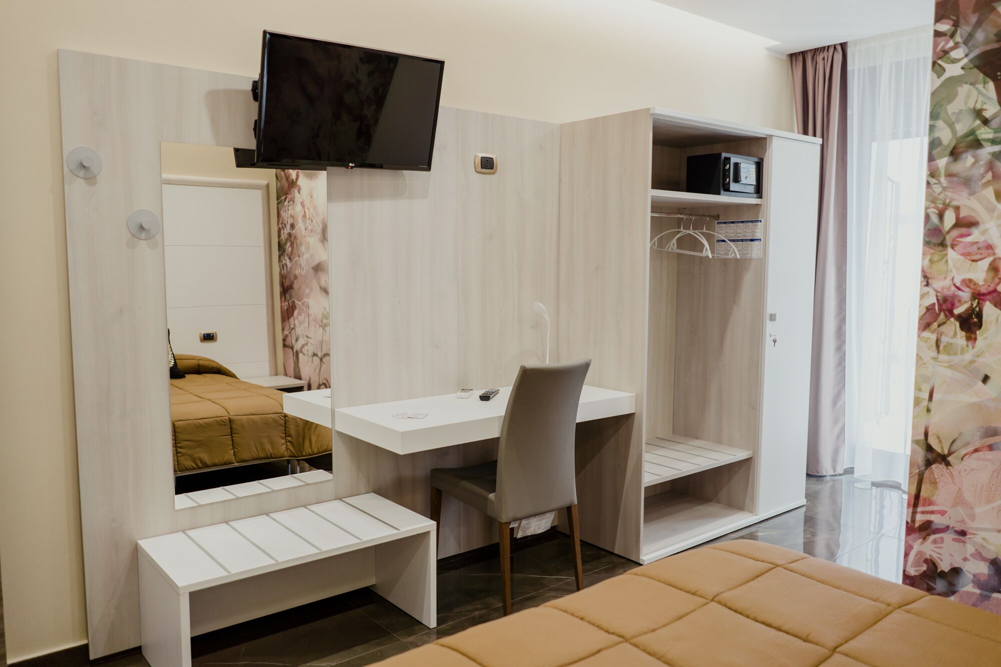 A compact hotel room with a bed, a desk, a chair, a TV, and a wardrobe.